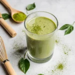 Creamy matcha protein shake in glass with matcha powder on counter